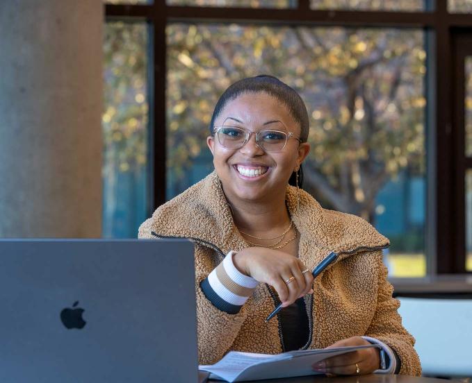 CU Denver student sitting at table with laptop smiling at camera