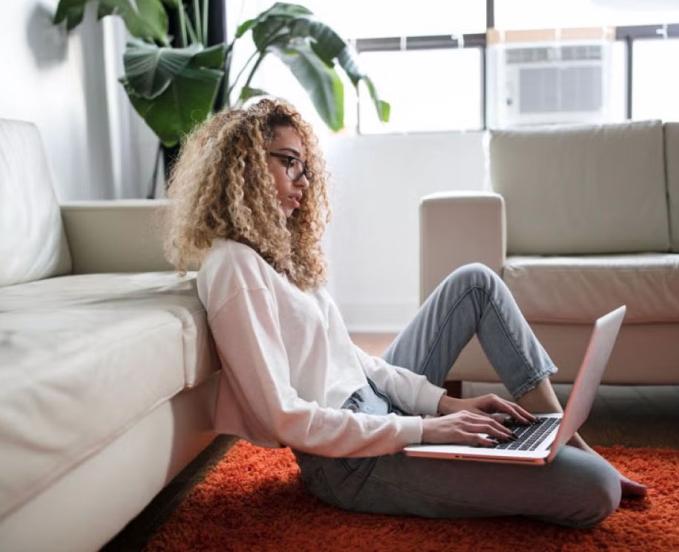 CU Denver online student using laptop sitting on rug