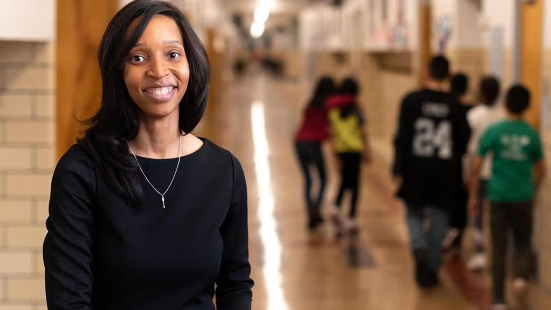 Professional woman standing in hallway with students walking to class in background