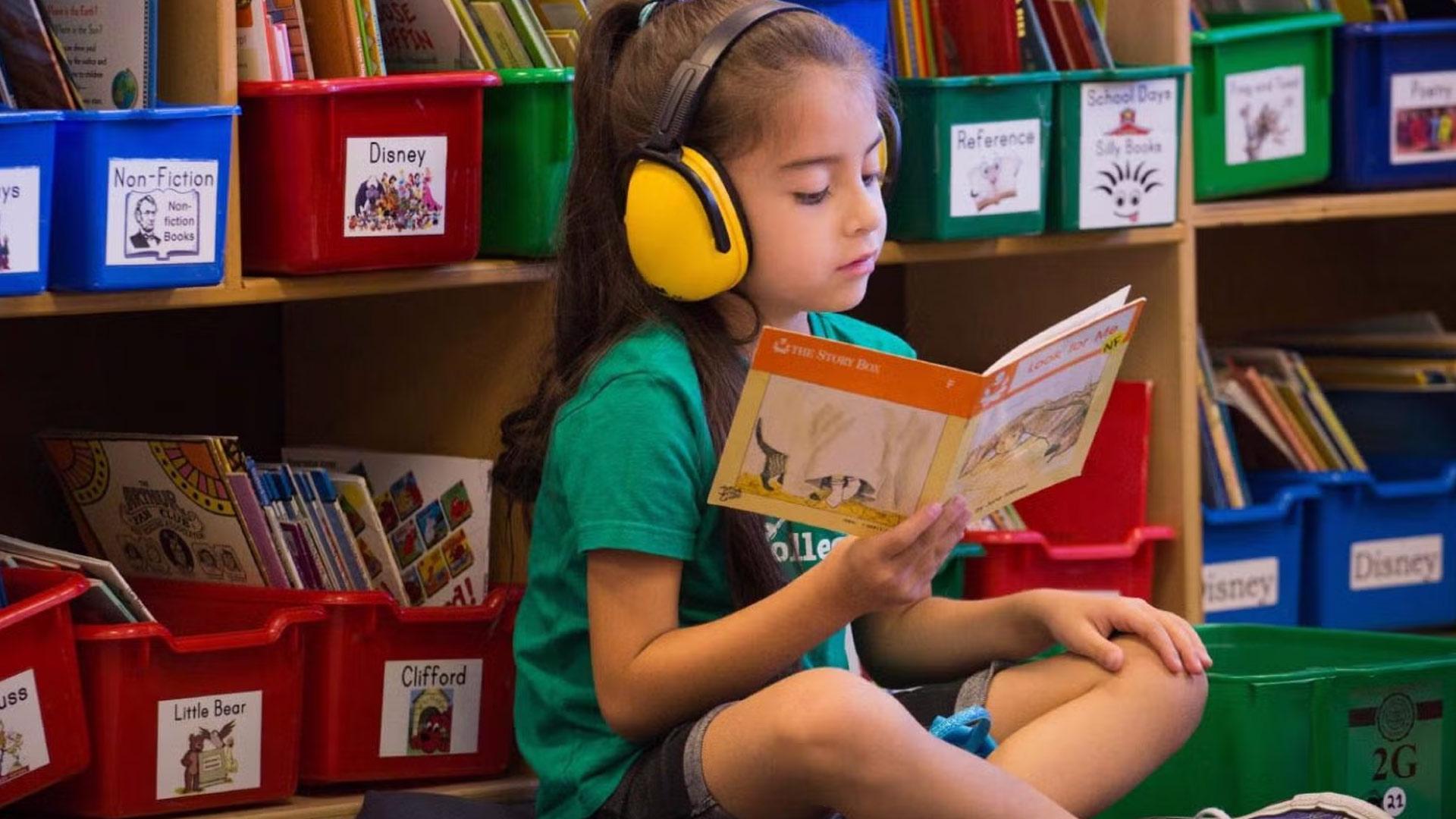 Child reading book in library floor while wearing noise cancelling headphones