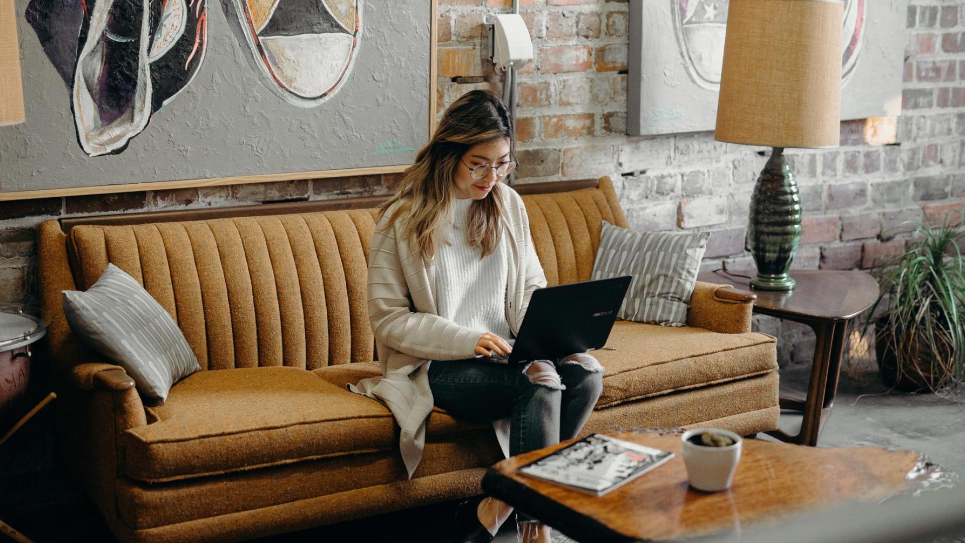 CU Denver Online student sits comfortably on a couch in a café, focused on her laptop, seamlessly balancing work and studying at her convenience.