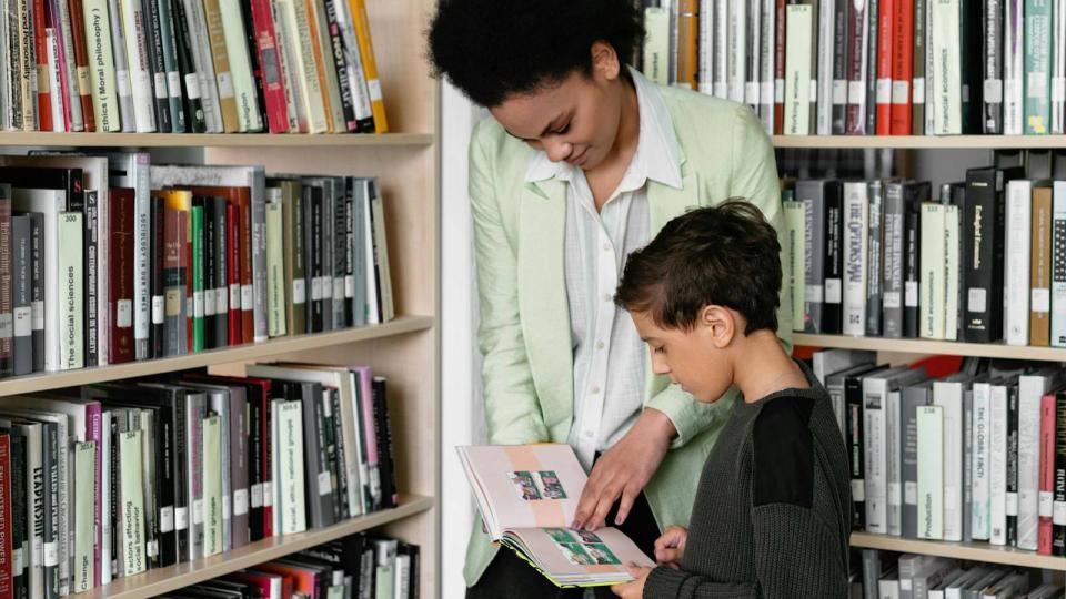 Librarian working with student reading book in library