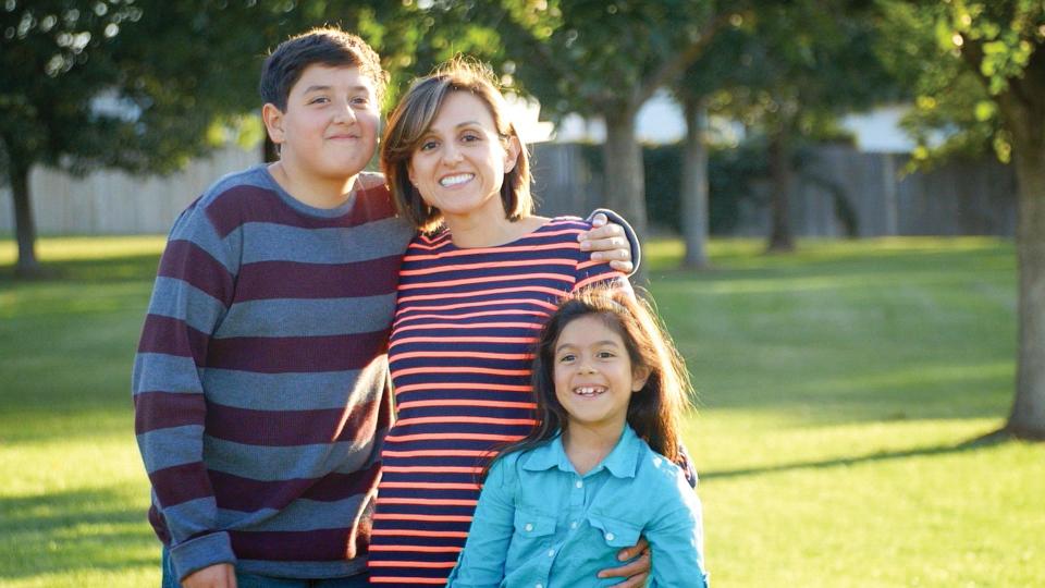 A woman who is a past CU Denver HDFR student smiles with two children in a sunny park.