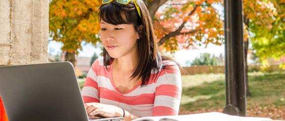 CU Online student working outside on a laptop computer.