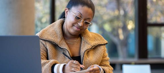 CU Denver online student taking notes with laptop