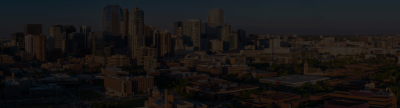 Ariel photograph of University of Colorado Denver in the foreground and downtown Denver in the background. The image is darkened so that text can overlay the image.