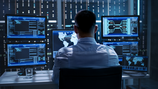 Cybersecurity professional works on computer with multiple monitors.